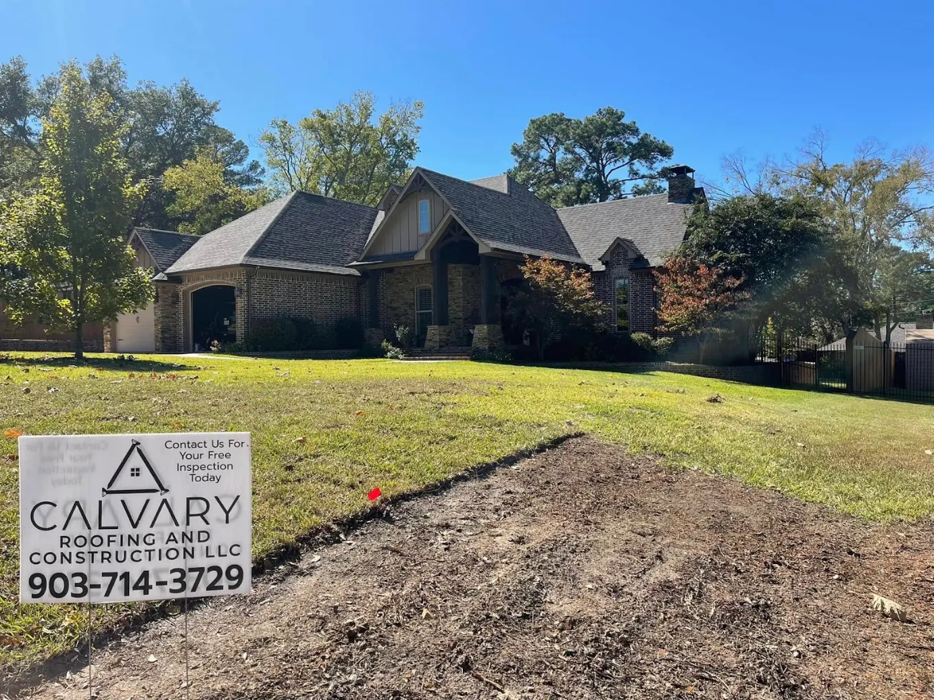 Completed roof replacement on a large East Texas home with a Calvary Roofing and Construction yard sign in the yard